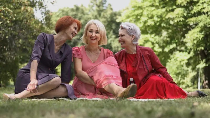 Drei Frauen sitzen lachend gemeinsam auf einer Wiese